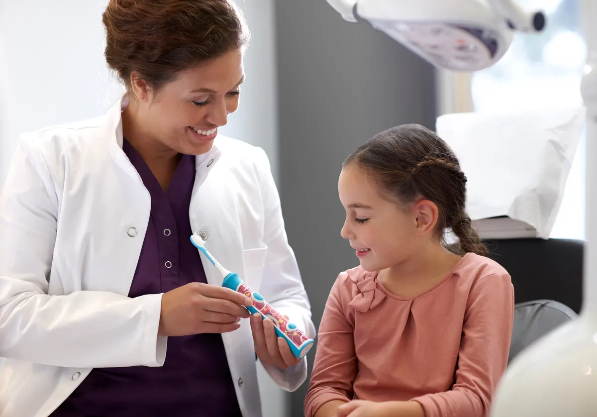 A dentist showing a young girl how to brush her teeth